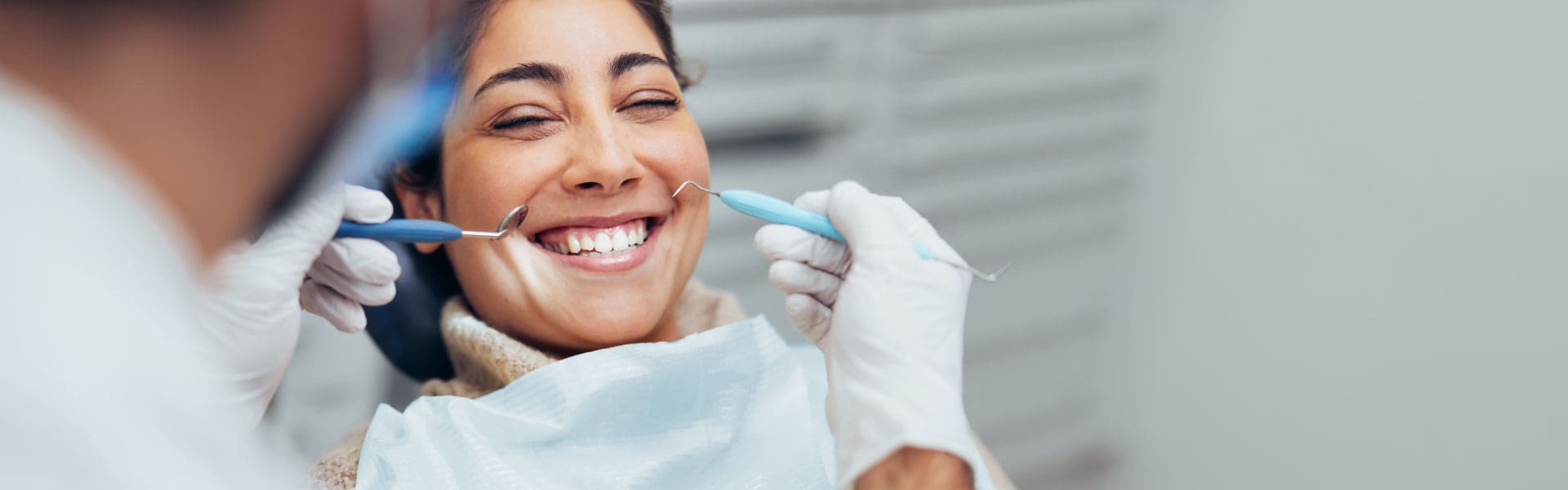 Sand-Creek-Crossing-Page-Banner-Brentwood-Hills-Modern-Dentistry A woman with a bright smile as a dentist uses dentistry tools